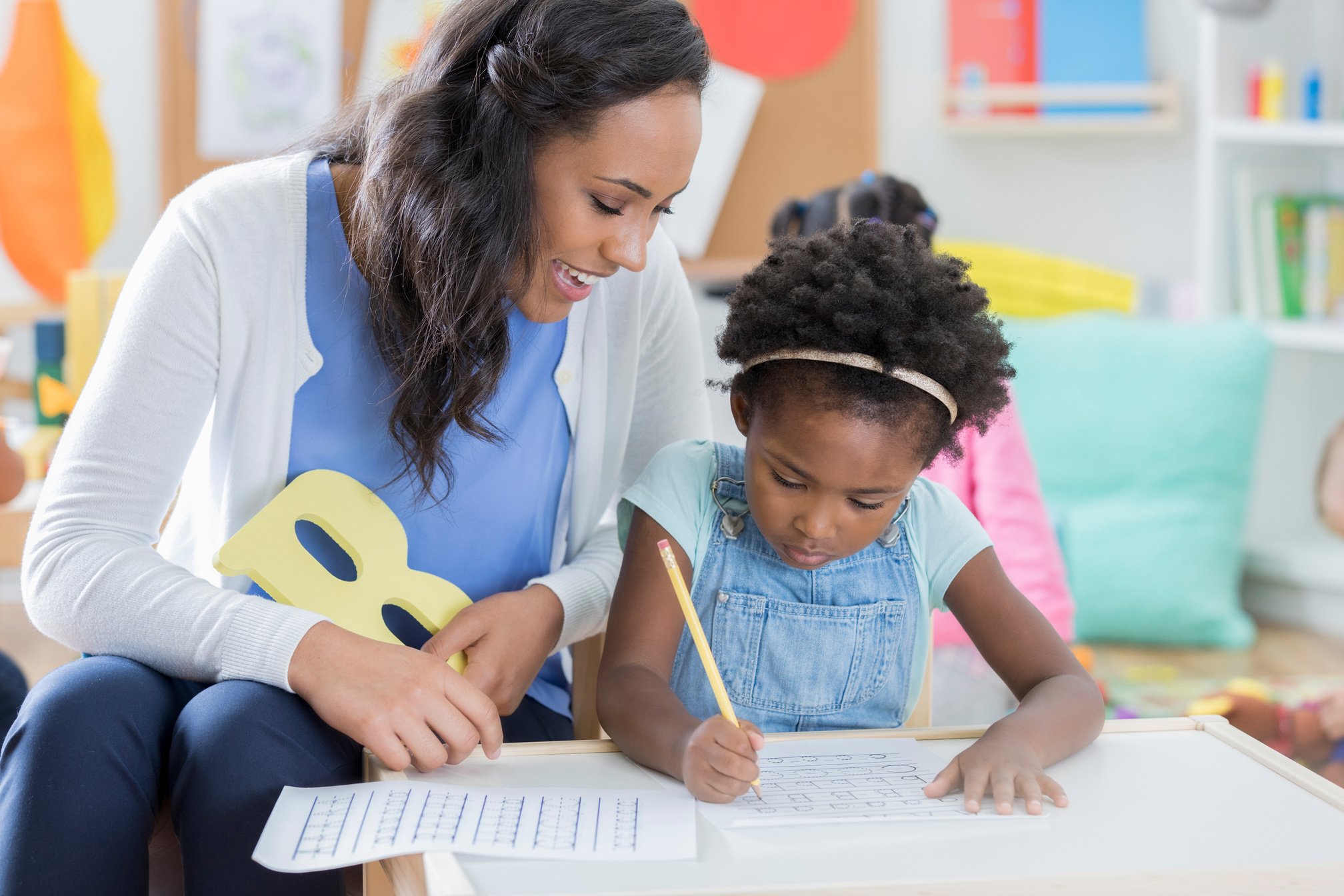 Child care worker helps little girl with handwriting